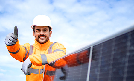 Portrait of professional worker standing by solar panel and holding thumbs up. Installation of solar power plant. Sustainable energy source.